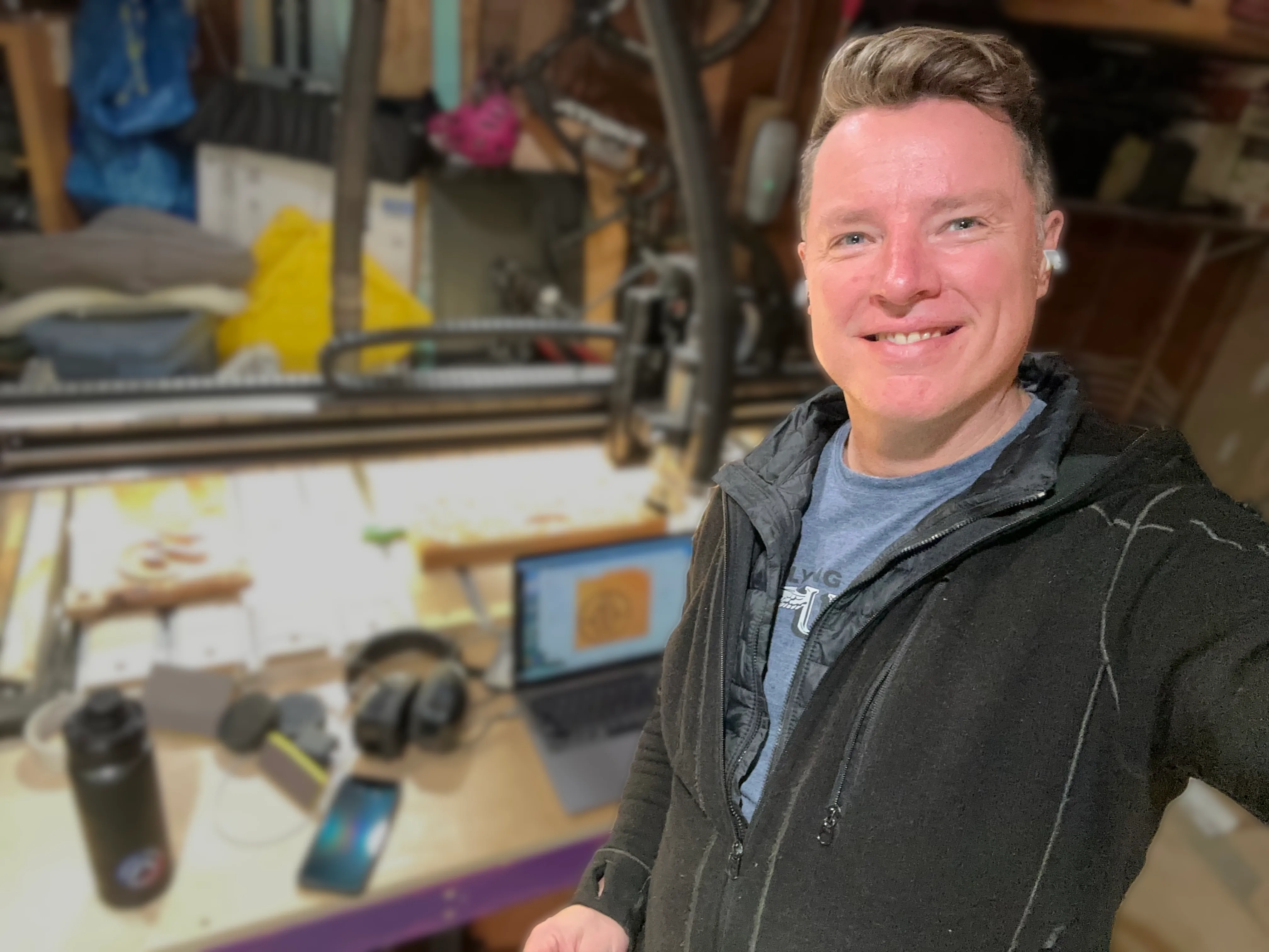 Kirk Hutton smiling beside his CNC router, with the Port Moody Woodcraft logo on a laptop screen behind him